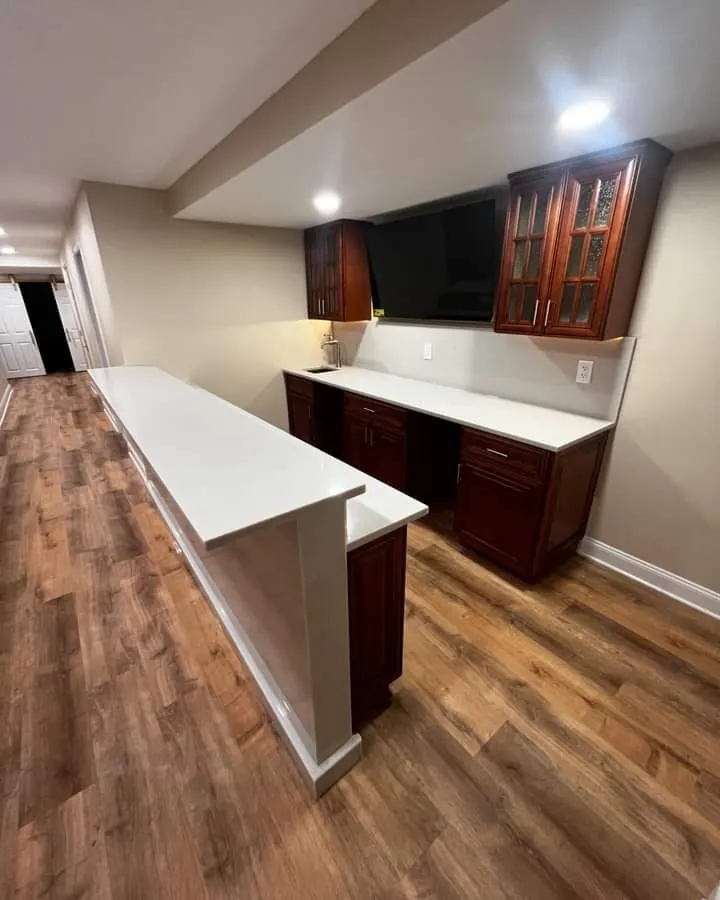 A bar with cherry cabinets, glass-front uppers and a white quartz counter over vinyl plank flooring