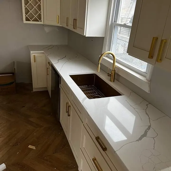 A kitchen with white shaker cabinets, a white quartz countertop and a brass faucet over a steel sink