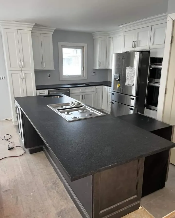 A kitchen with white cabinets, a stainless fridge and a large island with a black countertop and a gas cooktop