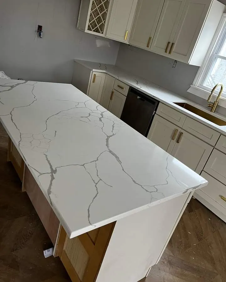 A white quartz countertop with grey veining on white cabinets, over a wood floor