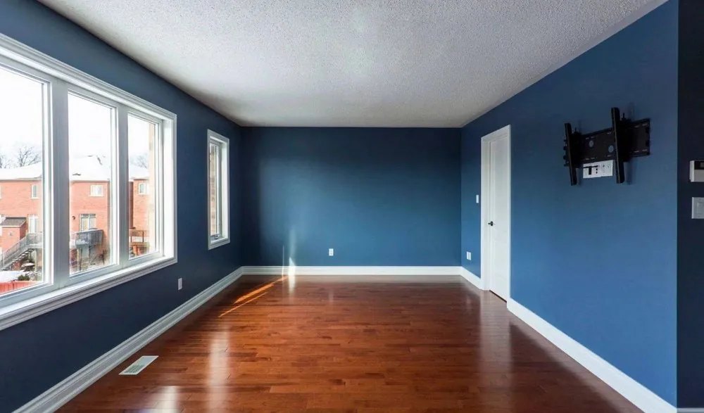 An empty bedroom painted deep blue with white trim and a wood floor